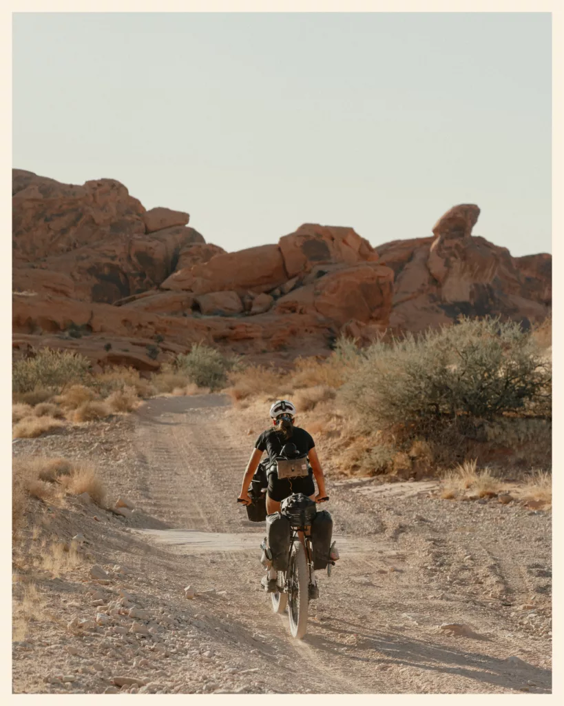 Bikepacker sur une piste sableuse entre les rochers rouges du Nevada