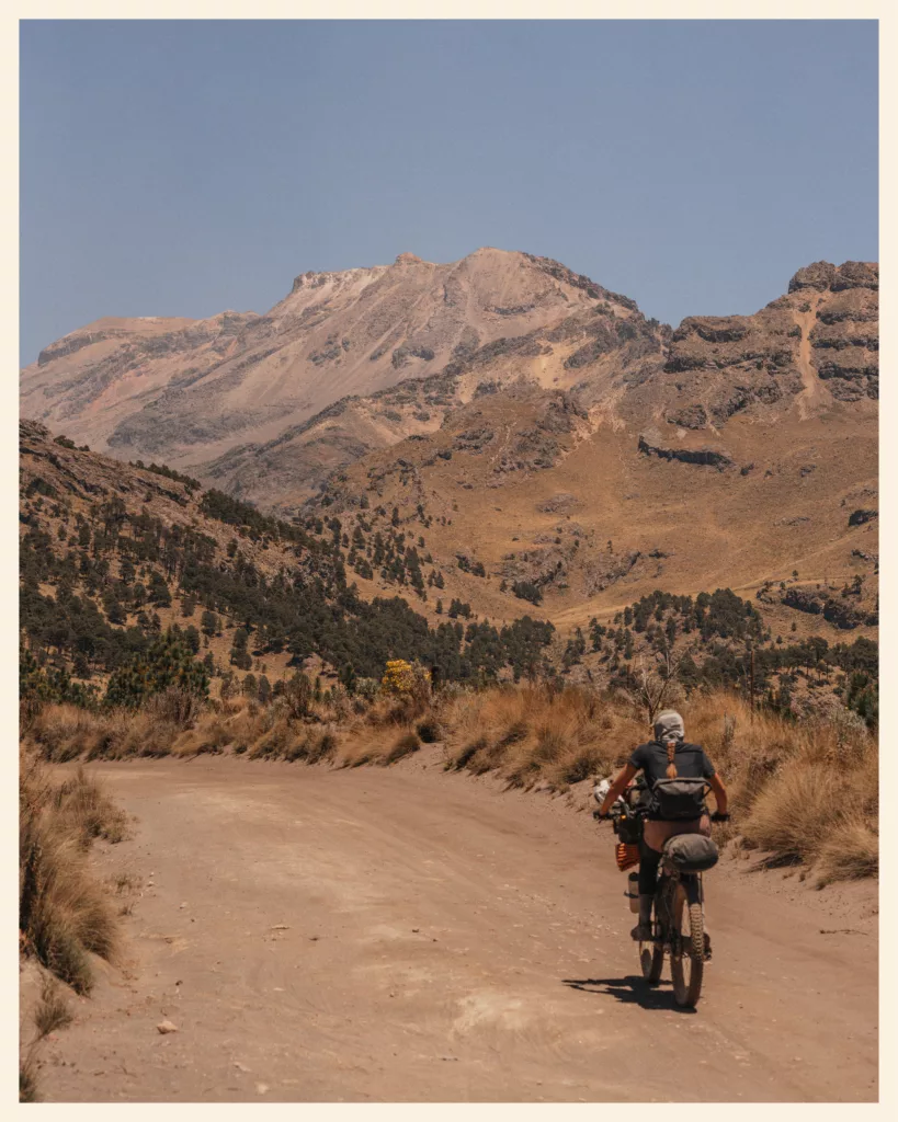 Bikepacker sur une piste de terre au pied d'un volcan, sur la TransMexico Sur