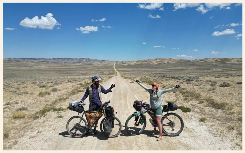 Nunzio et Annie, bras levés près de leurs vélos chargés, sur une piste désertique